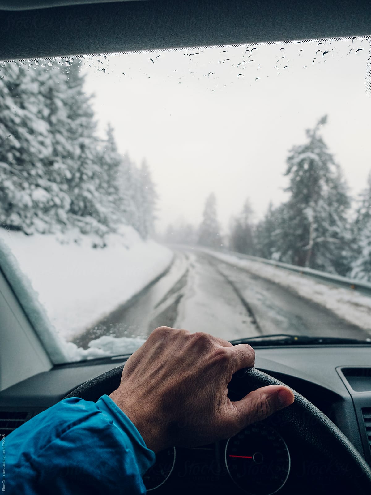 Anonymous man traveling and holding hands on the wheel driving on the snowy road mountain