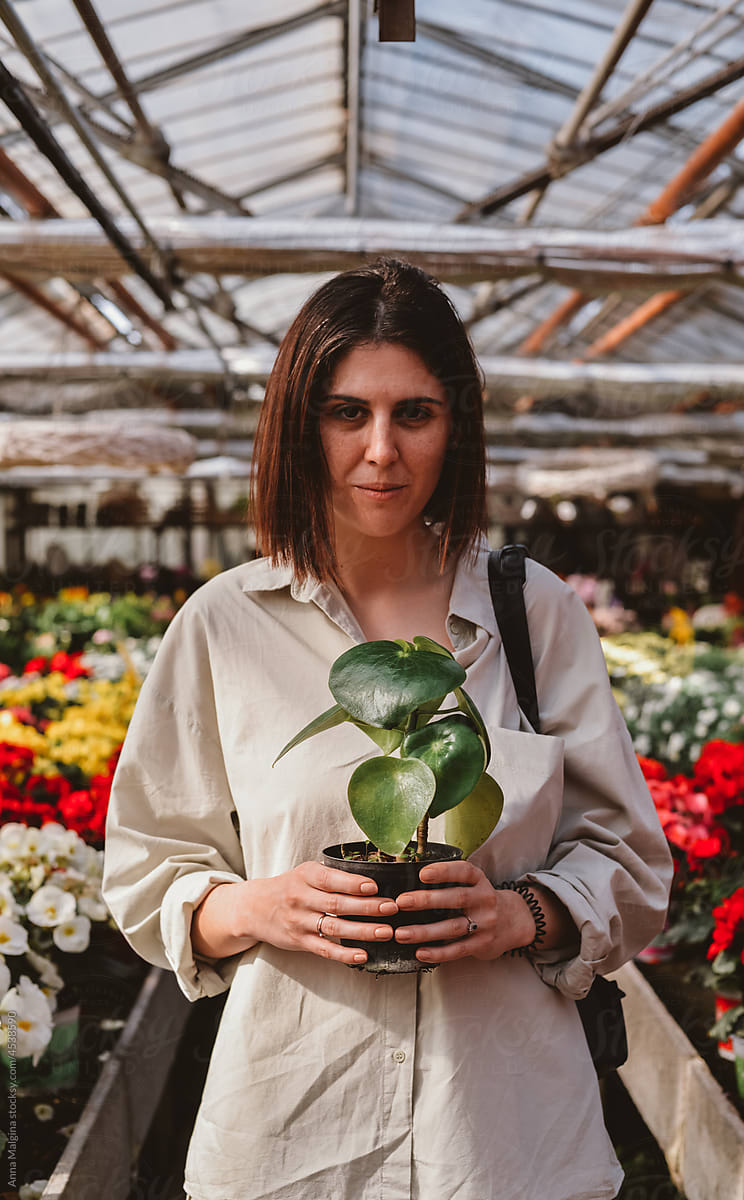 A woman in a sunny greenhouse with a green houseplant