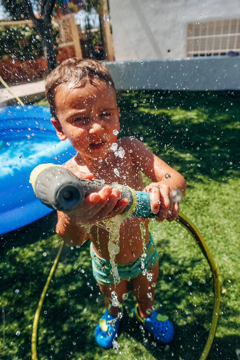 Boy playing with water hose in yard on summer day