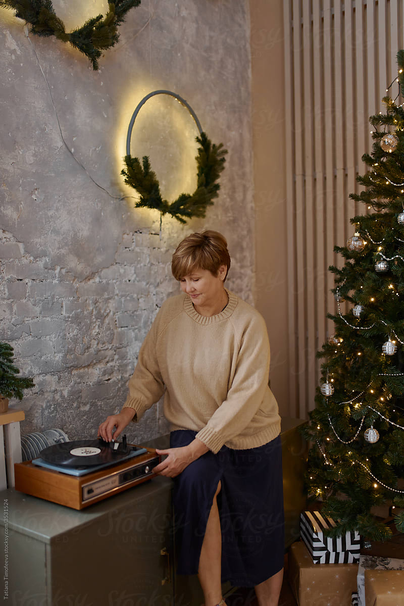 an adult woman listens to music on a vinyl record near the Christmas tree at home