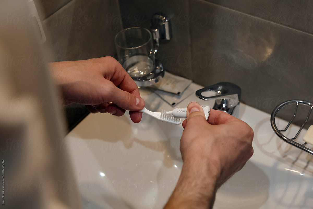 Crop faceless man putting single use toothpaste on toothbrush above sink
