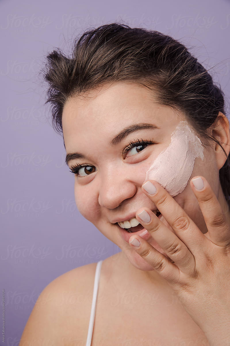 East asian model applying pink clay mask on her face smiling