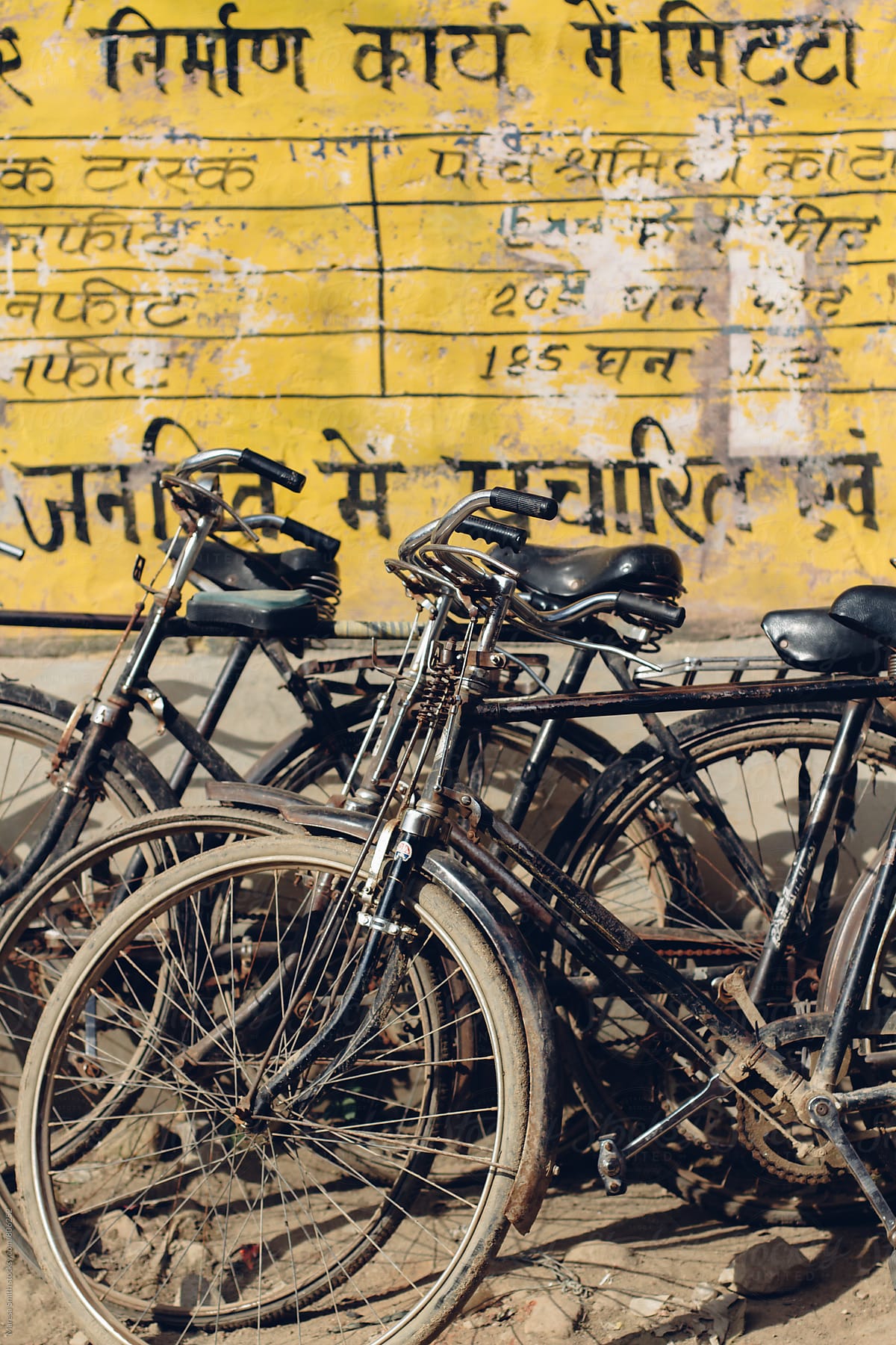 Dusty black bikes leaning on a yellow wall in India