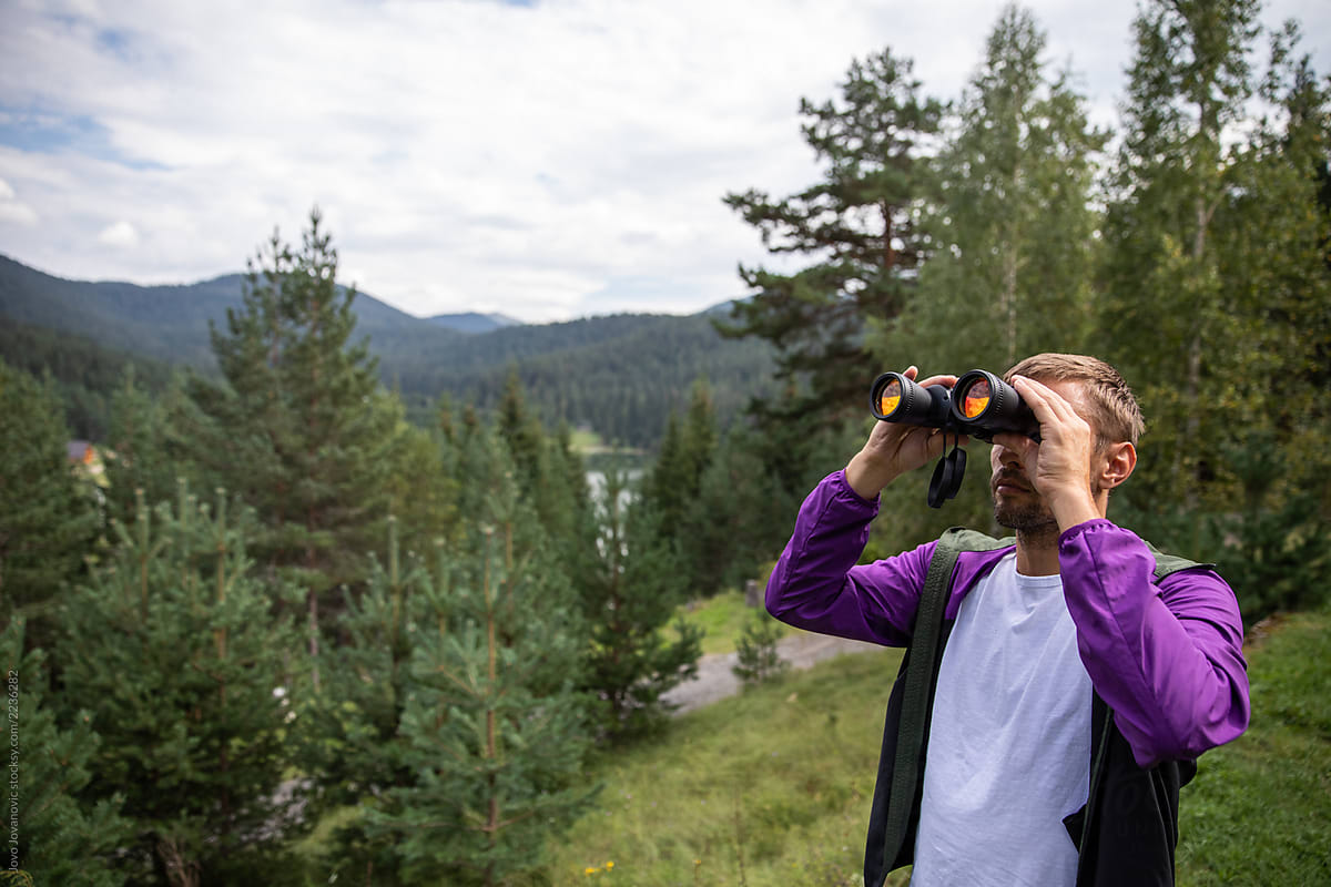 A man looking through binoculars in the mountains
