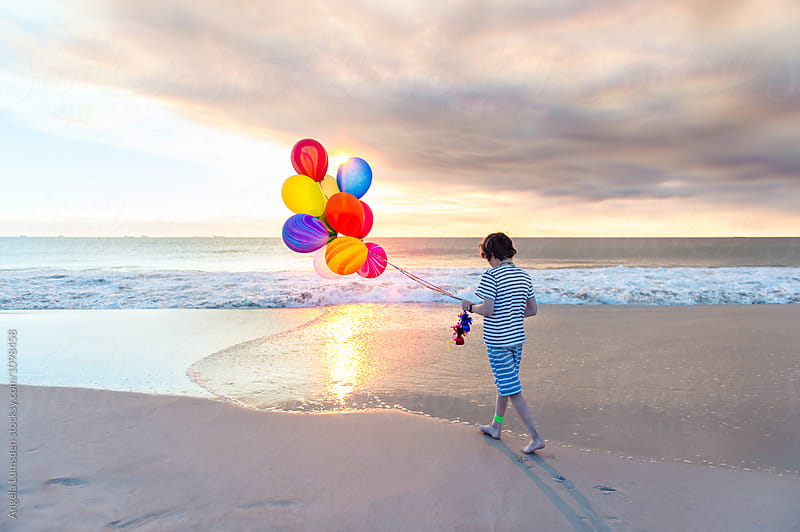 Boy with a bunch of colorful balloons, walking at the beach