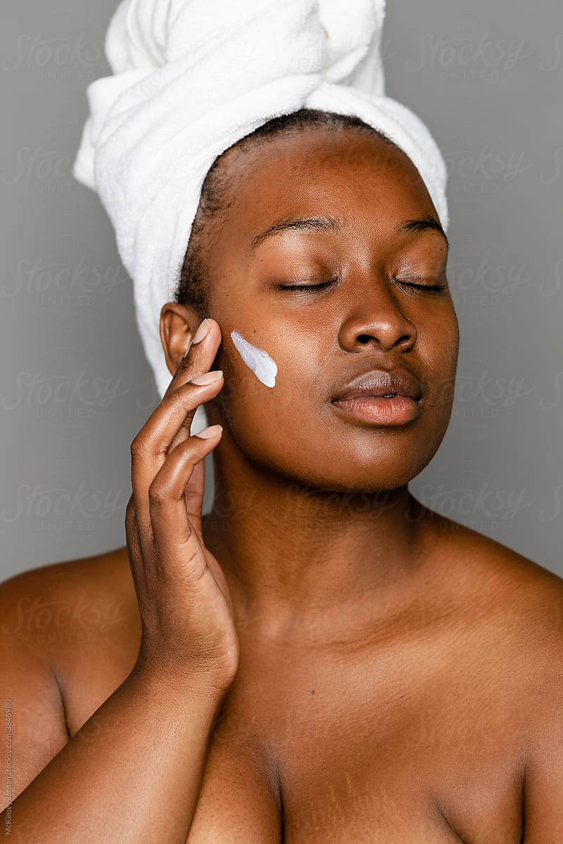 Woman With Eyes Closed Using Fingers To Apply Lotion
