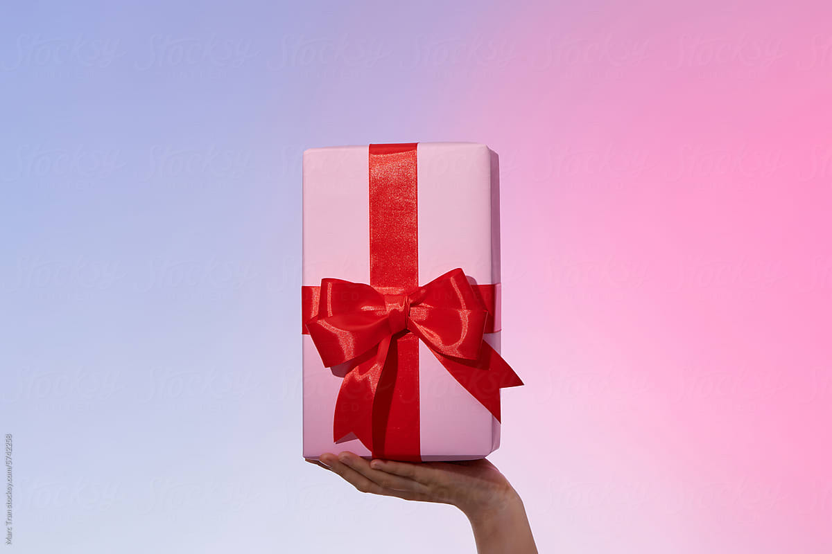Female hands hold a pink gift box with a red bow and slide it up