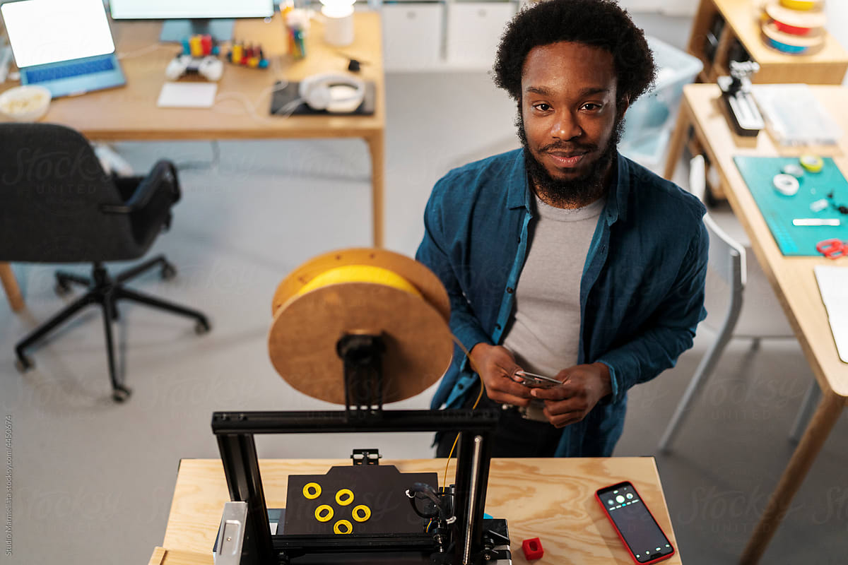 Happy male designer standing near 3D printer in studio