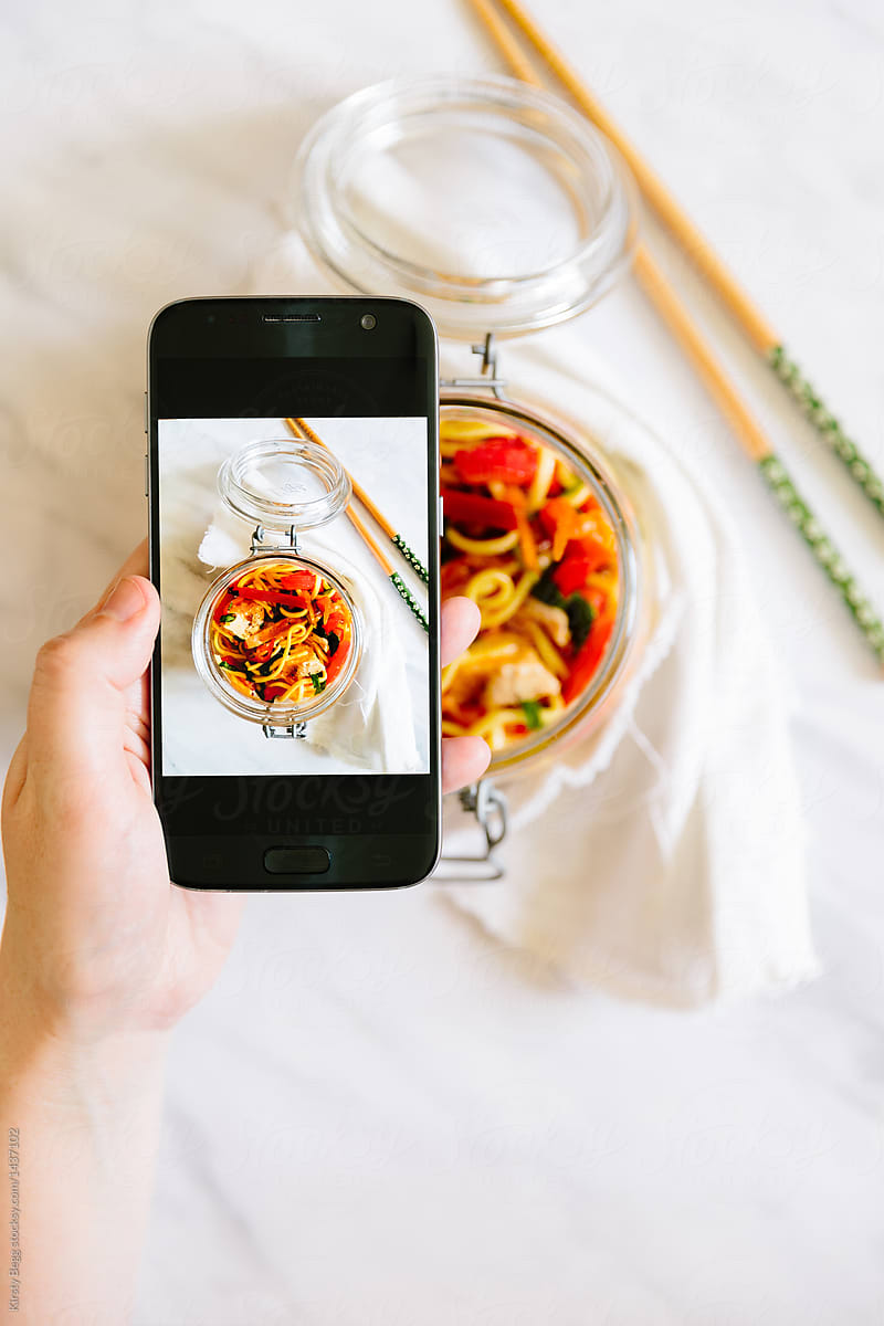 Woman taking photo with smartphone of her lunch, noodle salad