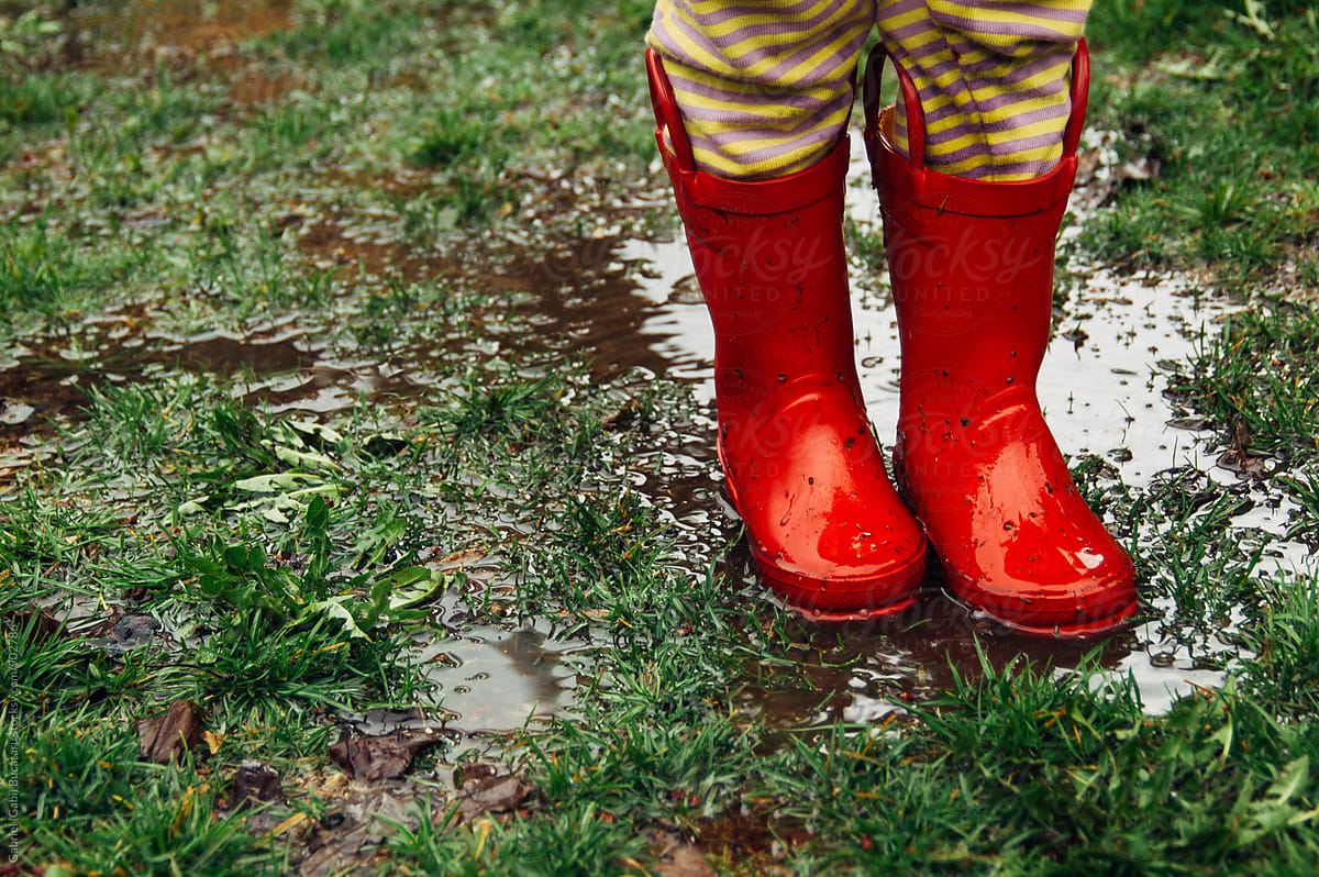 Child\'s feet in red rain boots on muddy grass