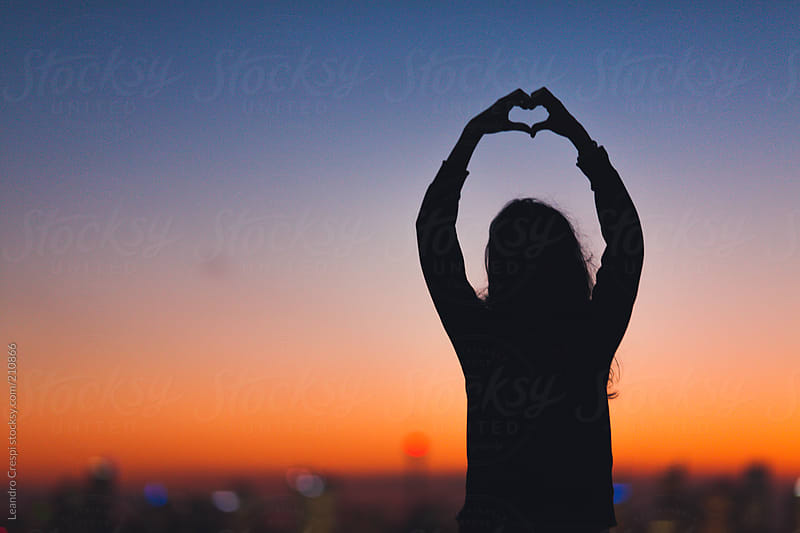 Woman In Silhouette Making Heart Shape With Hands On Sunset By Leandro