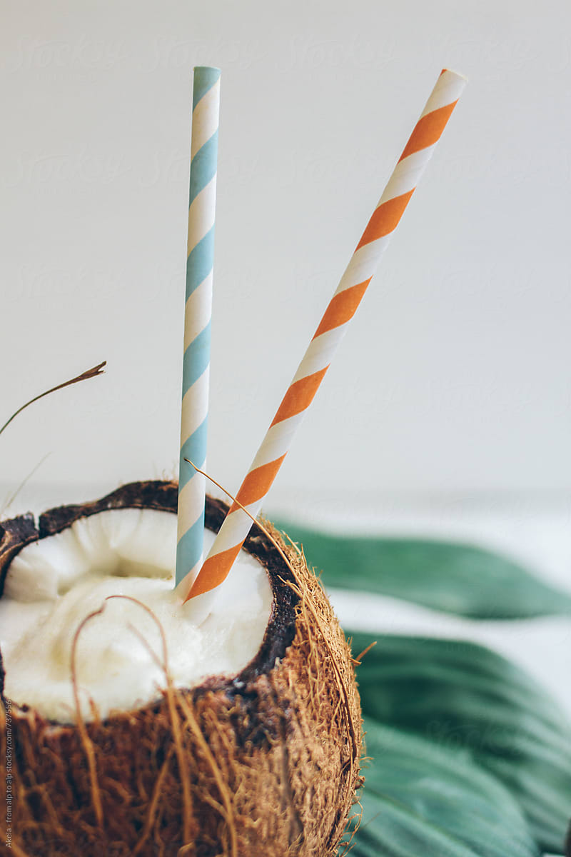 close up of a opened coconut filled with a pina colada and colorful drinking straws