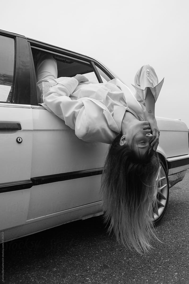 portrait of a girl in a white suit who climbed out of a car window, covering part of her face with her hand