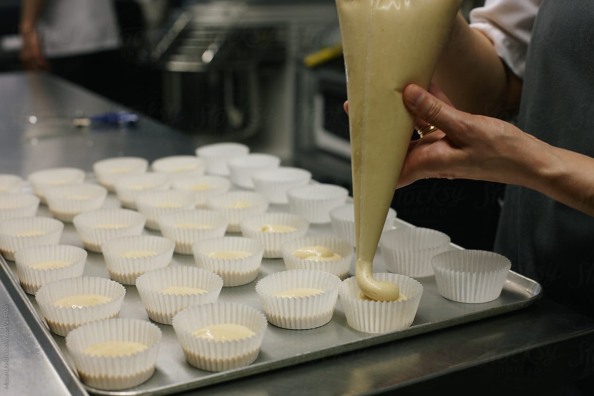 Baker filling with muffin batter a tray of molds