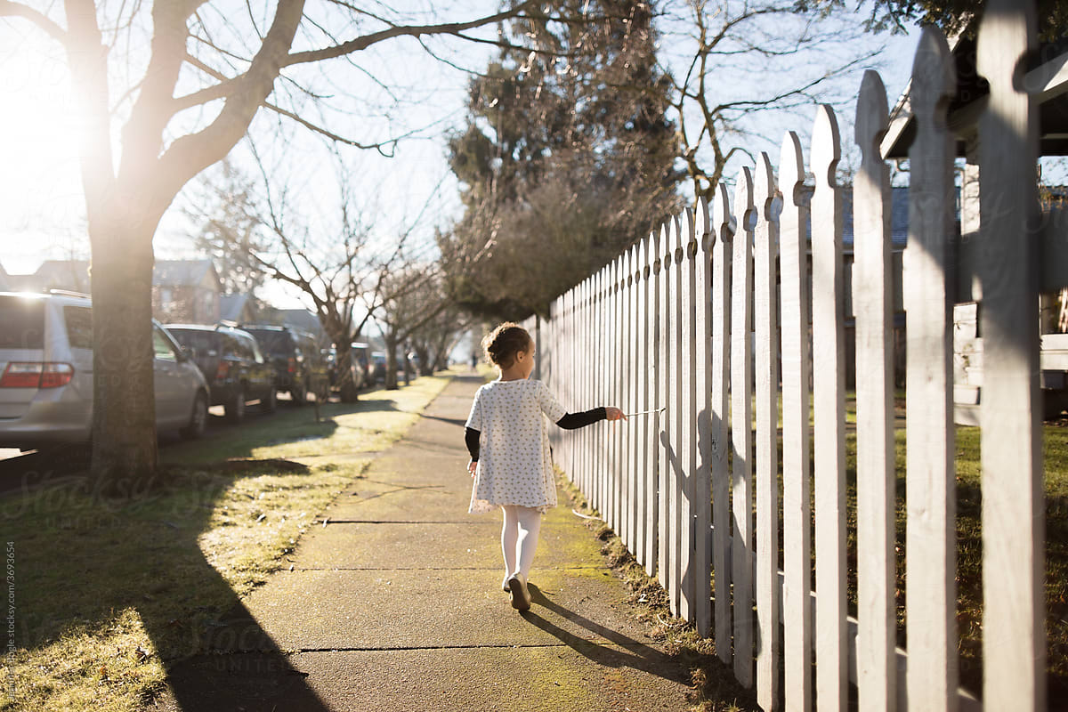 Girl walks near white picket fence