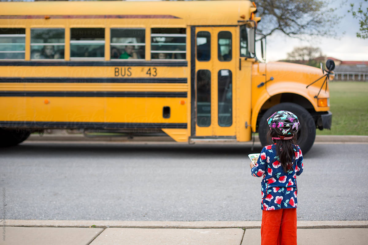 Little girl  holding a tray of cookies in front of a school bus