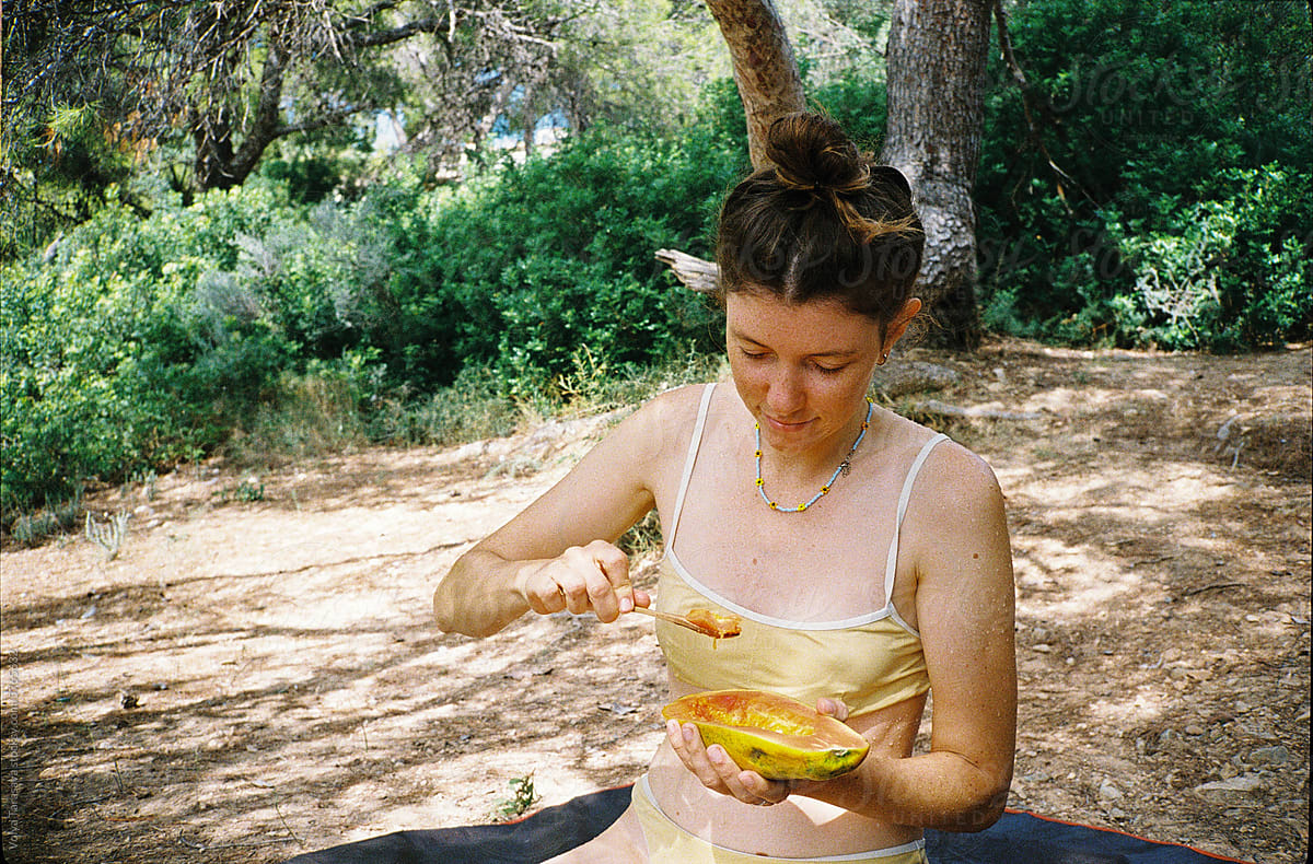 Young woman sitting in the forest and eating papaya