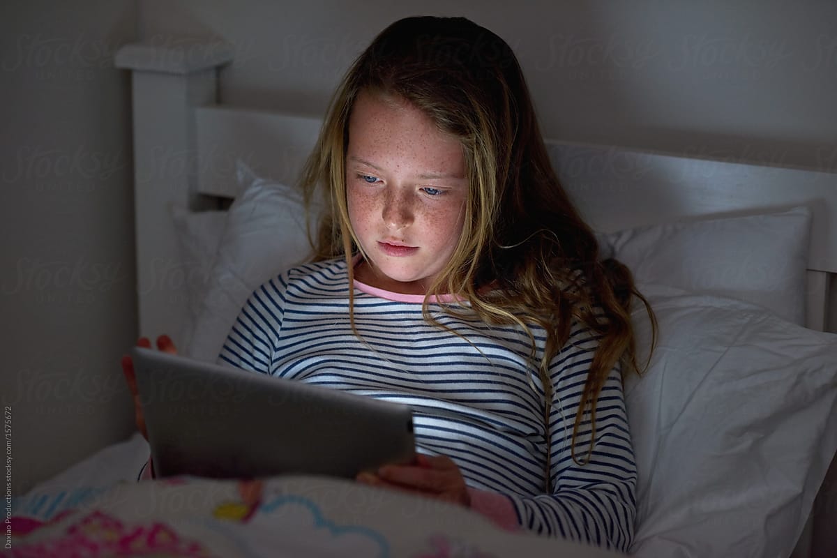 Girl looking at tablet device, face lit up in dark bedroom