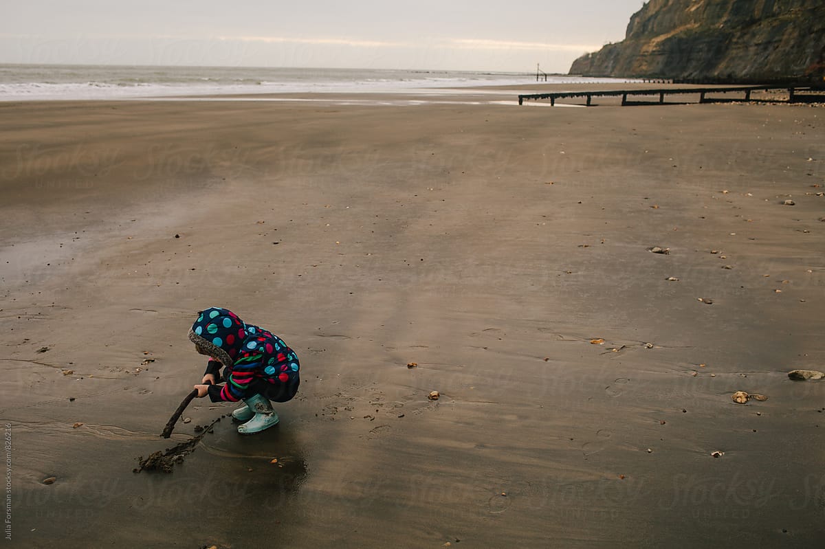 Little girl draws a line in the sand on an empty beach.