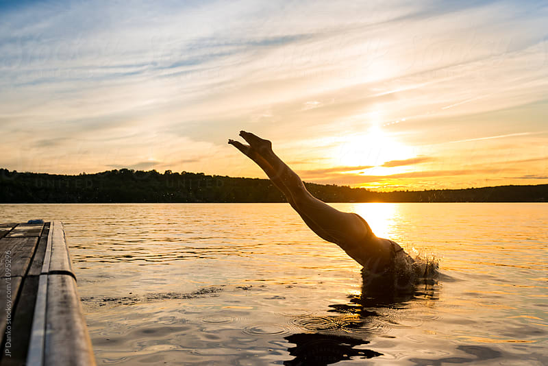 Woman Diving From Dock Into Warm Summer Cottage Lake At Sunset