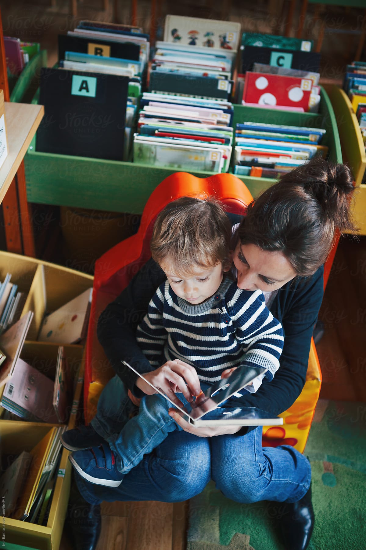 Cute baby boy and his mother reading a story in an old children library