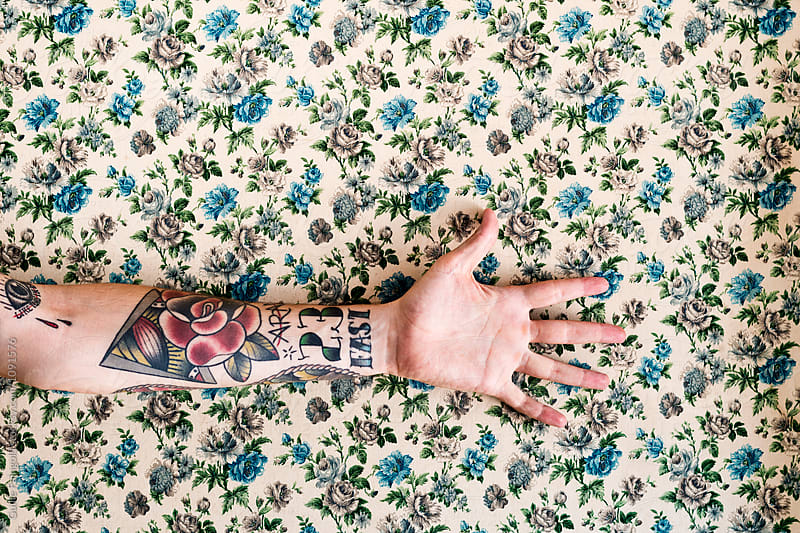 Tattooed male arm against of floral patterned wall