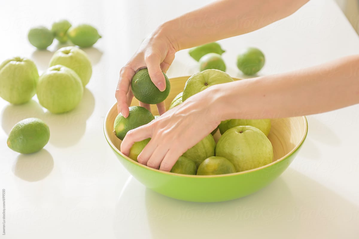 Young woman\'s hands sorting guava and lemon fruit on white kitchen table.