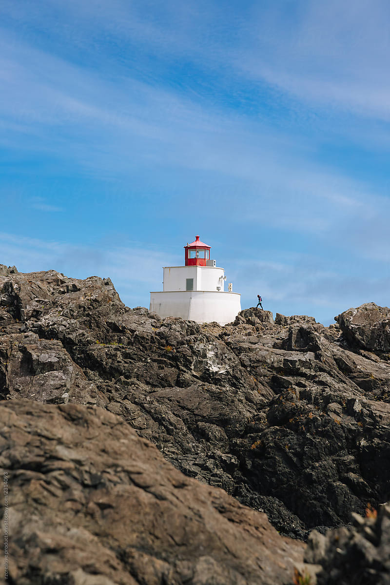Large lighthouse and  woman climbing rocky coastline.