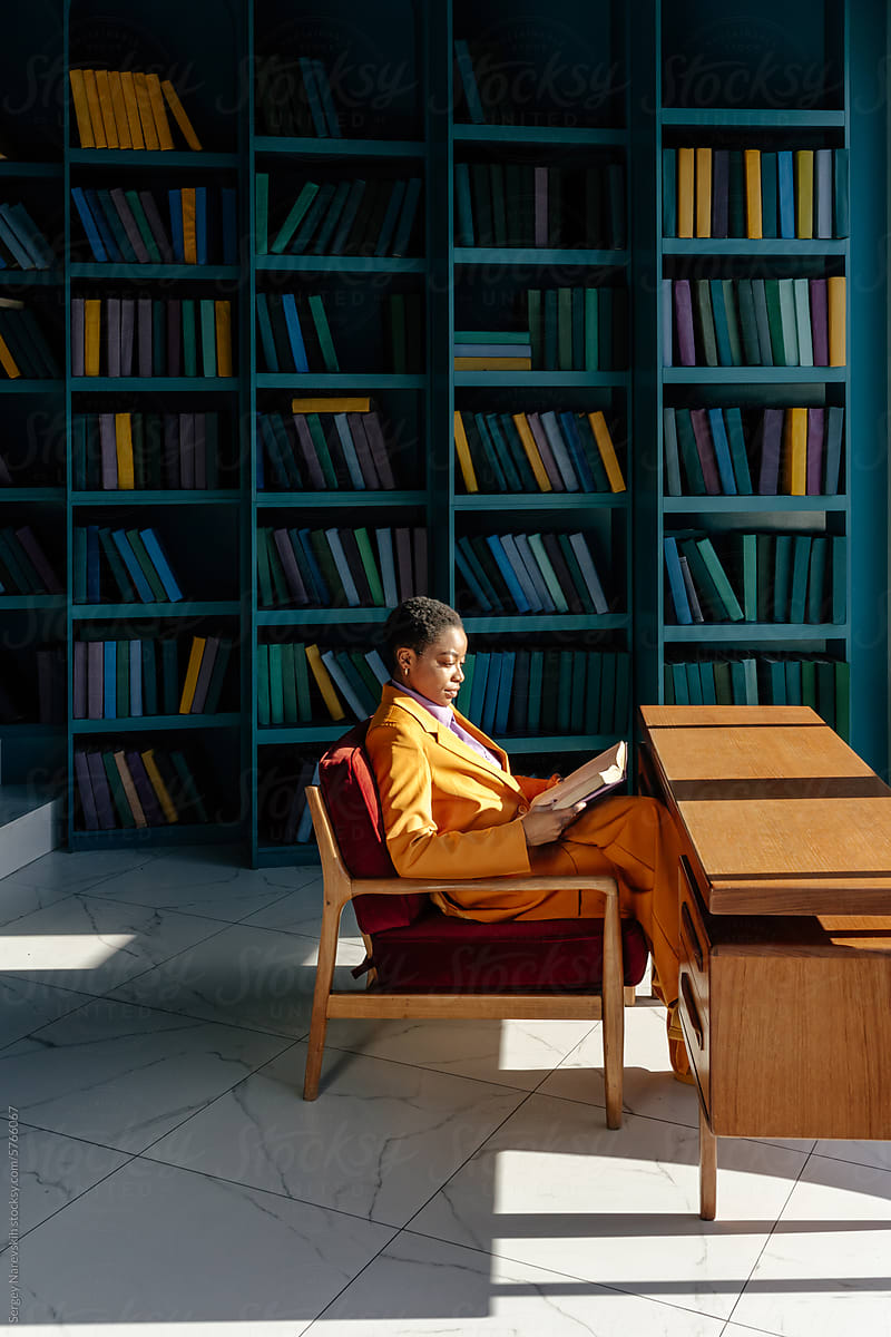 Focused black woman sitting and reading book in library