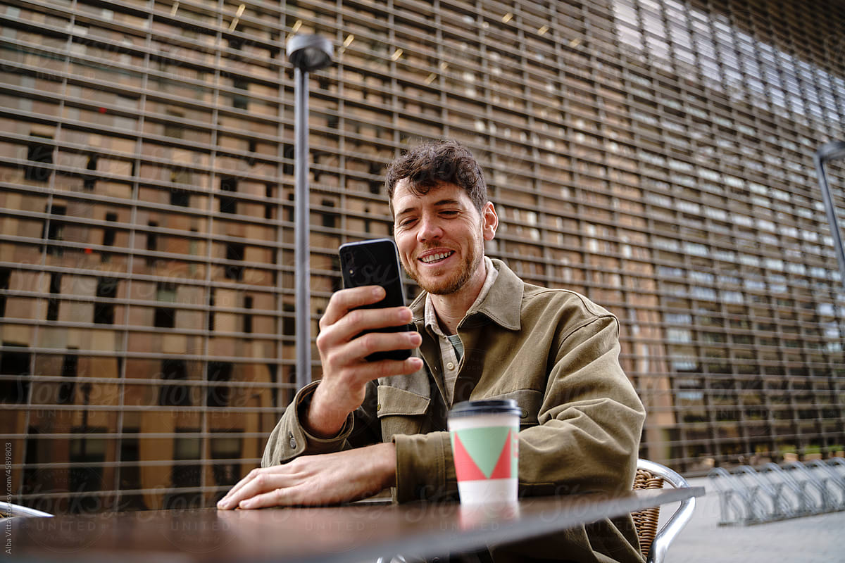 Joyful man with cell phone and coffee to go at city