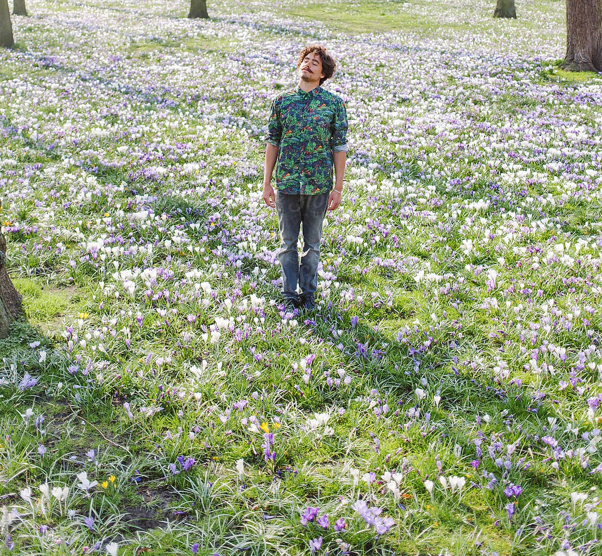 Young stylish man standing in a grass field of flowers with a flower shirt on.