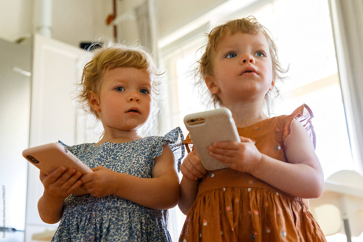 Little twins with smartphones at home