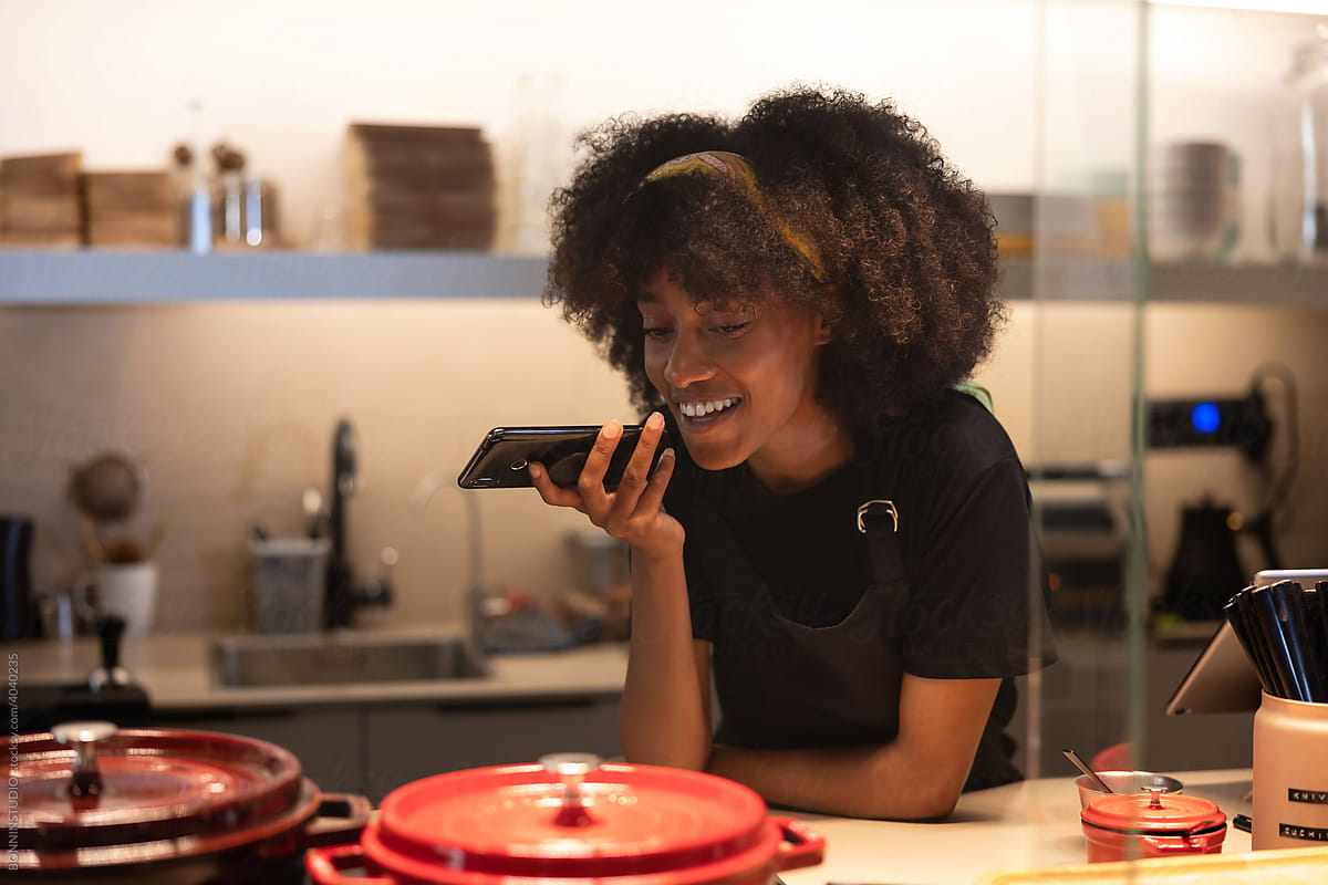 Smiling black waitress recording voice message on smartphone in cafe