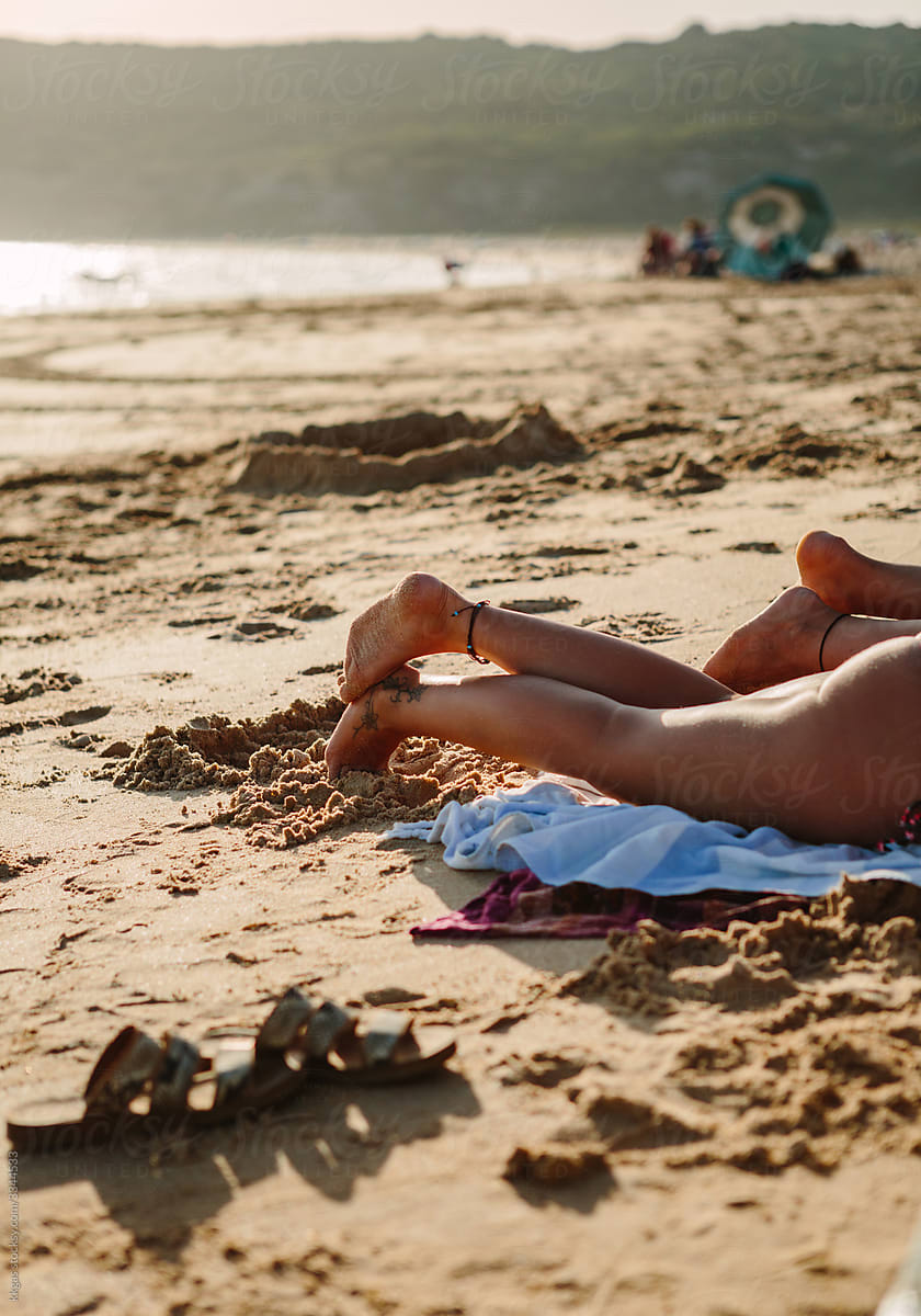 Two anonymous sunbathing womens legs on a beach