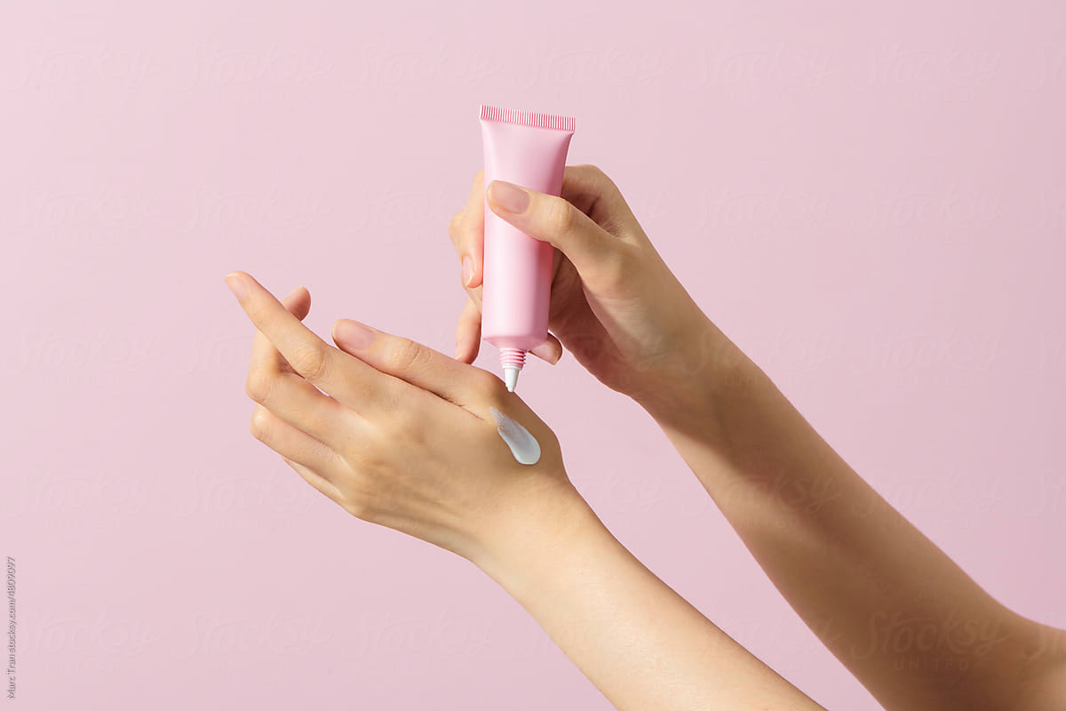 Women applying cream on the fingers isolated on a pink background.
