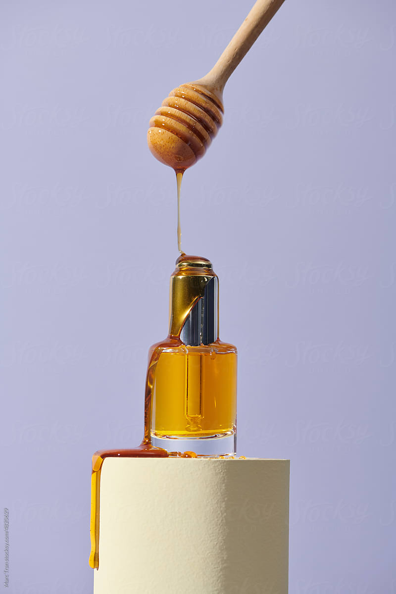 Pouring of honey from dipper onto bottle of essential oil