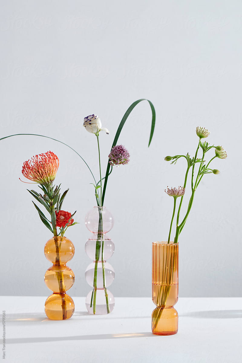 Bright wildflowers in bottles on white table, on light background