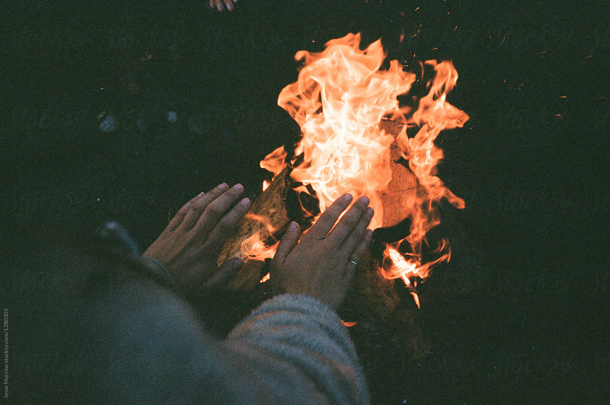 young woman warming hands over fire