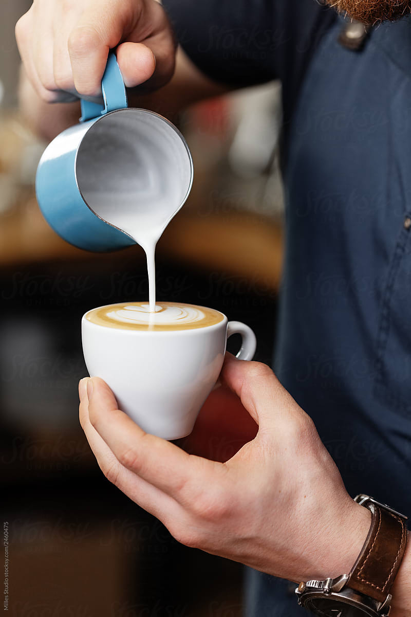 Crop barista preparing latte