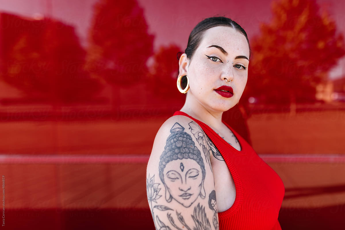 Tattooed woman looking at camera against red wall