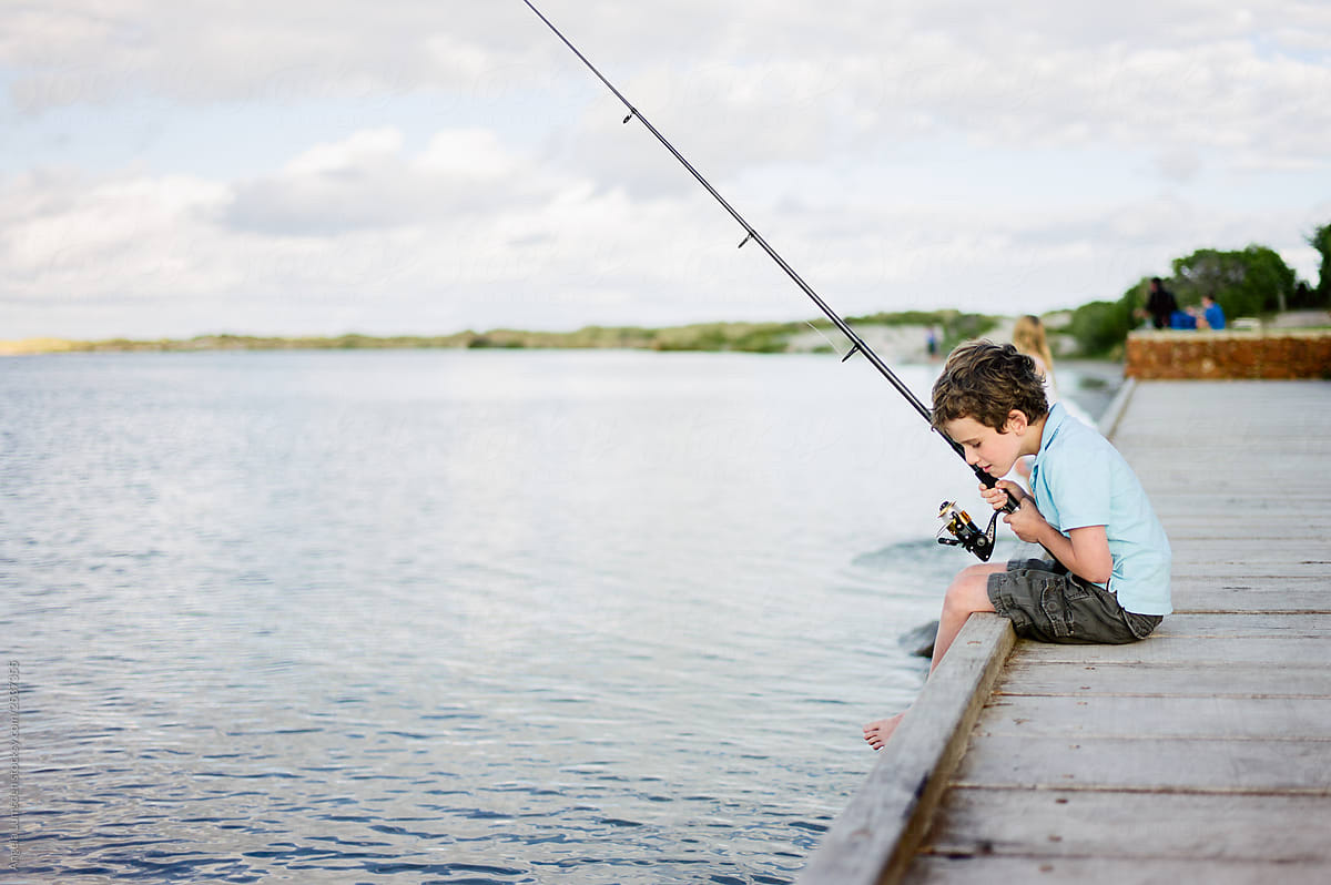 Young boy holding a fishing rod and sitting on a wooden dock