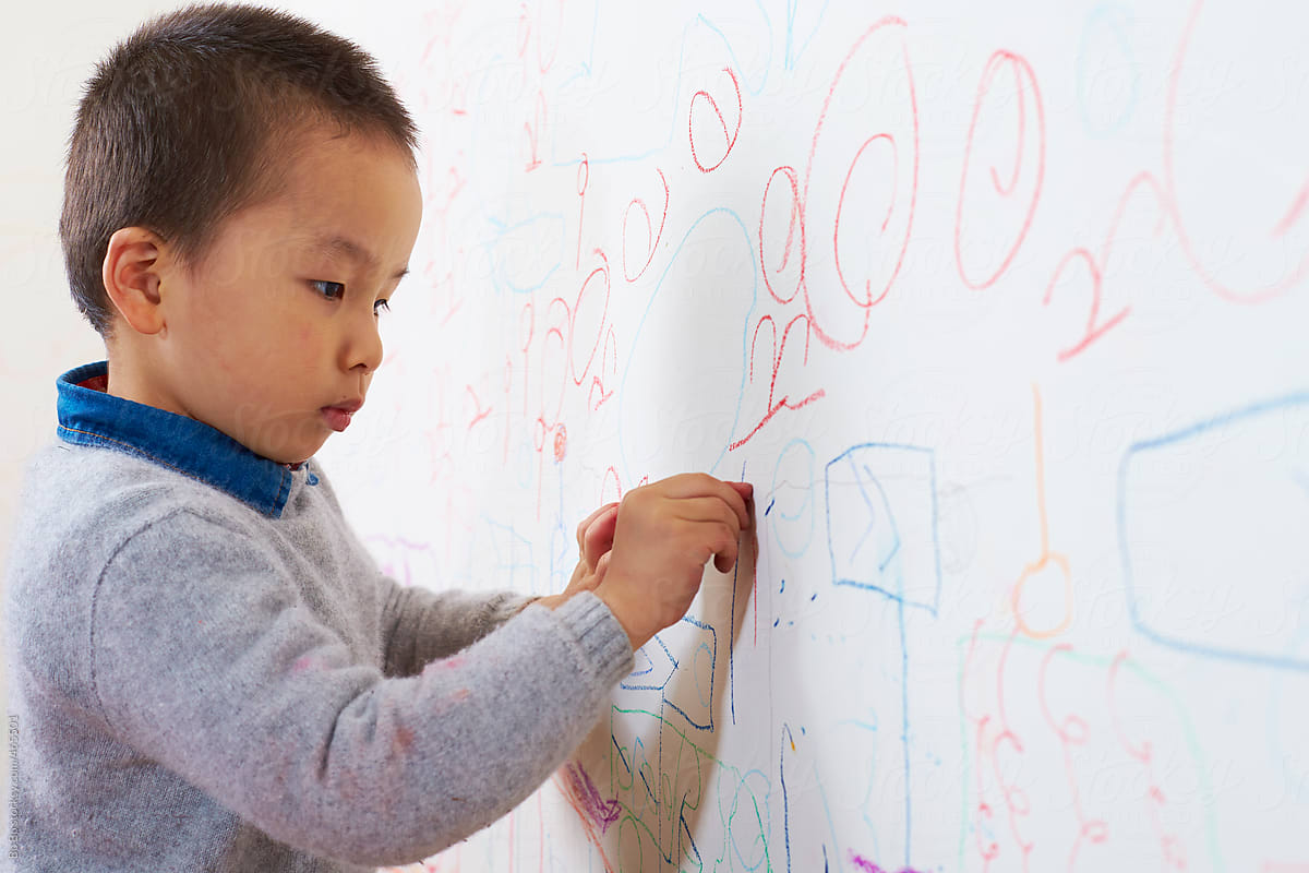little boy drawing picture on the wall