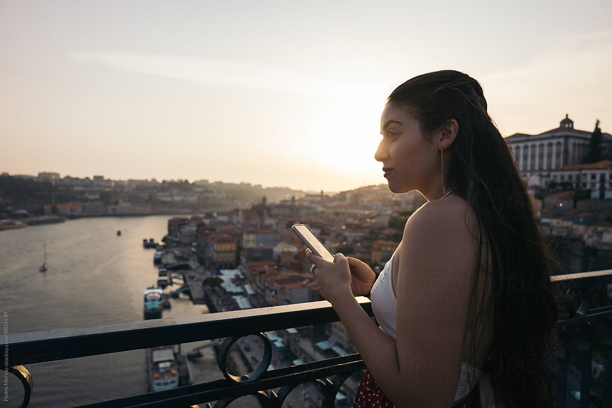 Young woman using smartphone and watching the city from the bridge