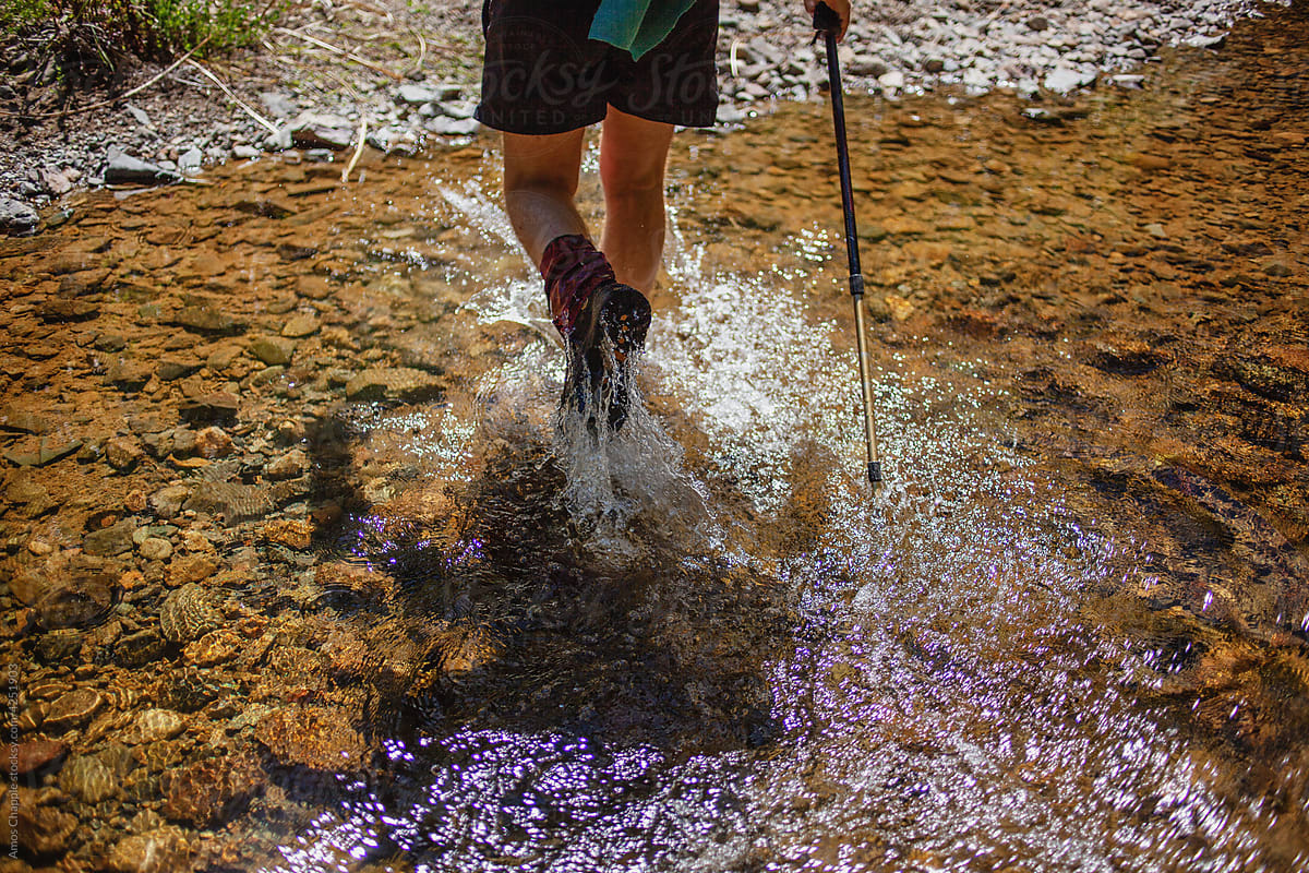 A hiker splashes through a shallow stream