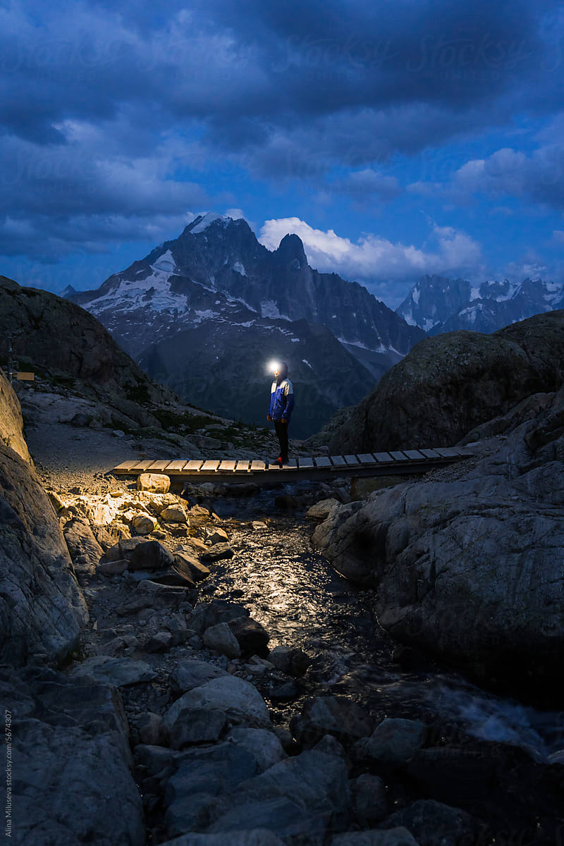 Man with headlamp against mountain peak at blue hour