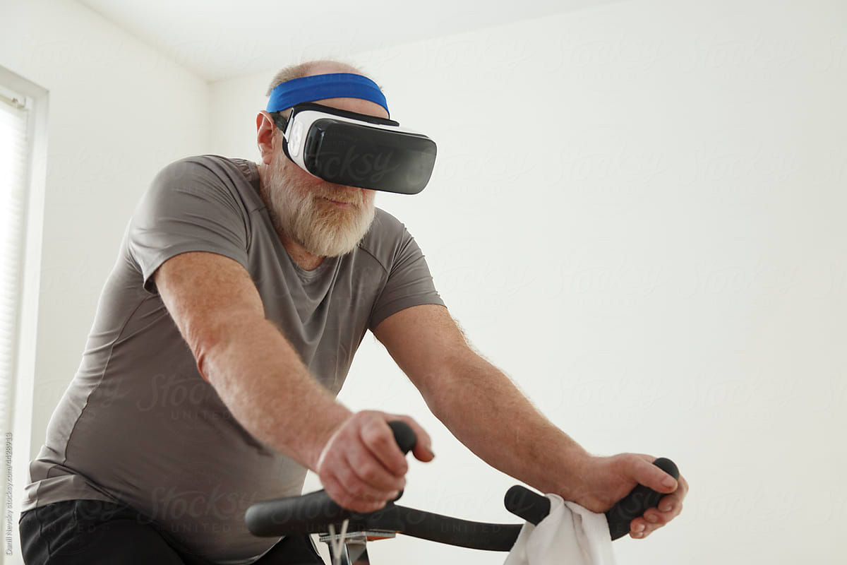 Elderly man in VR glasses training on cycling machine