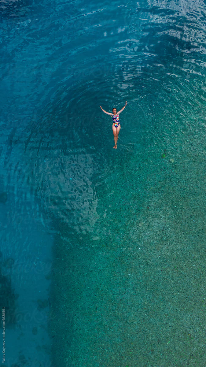 young woman relaxing in turquoise water, drone overhead