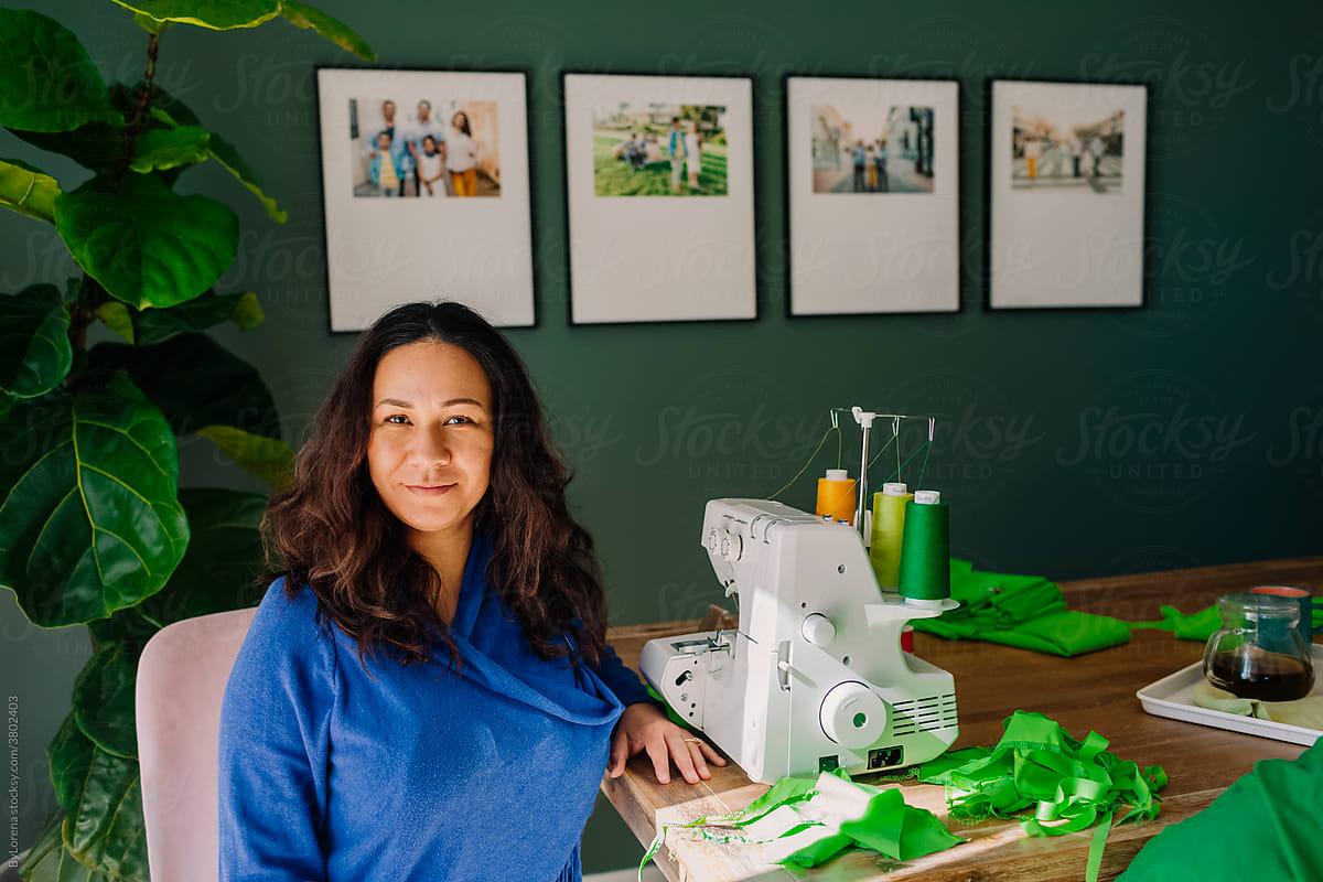 Portrait tailor woman next sewing machine and green garment