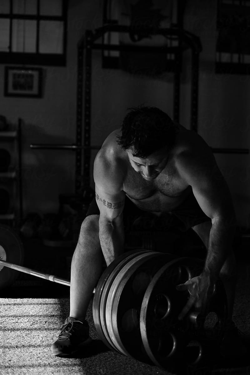 A shirtless man adds weight plates onto a barbell