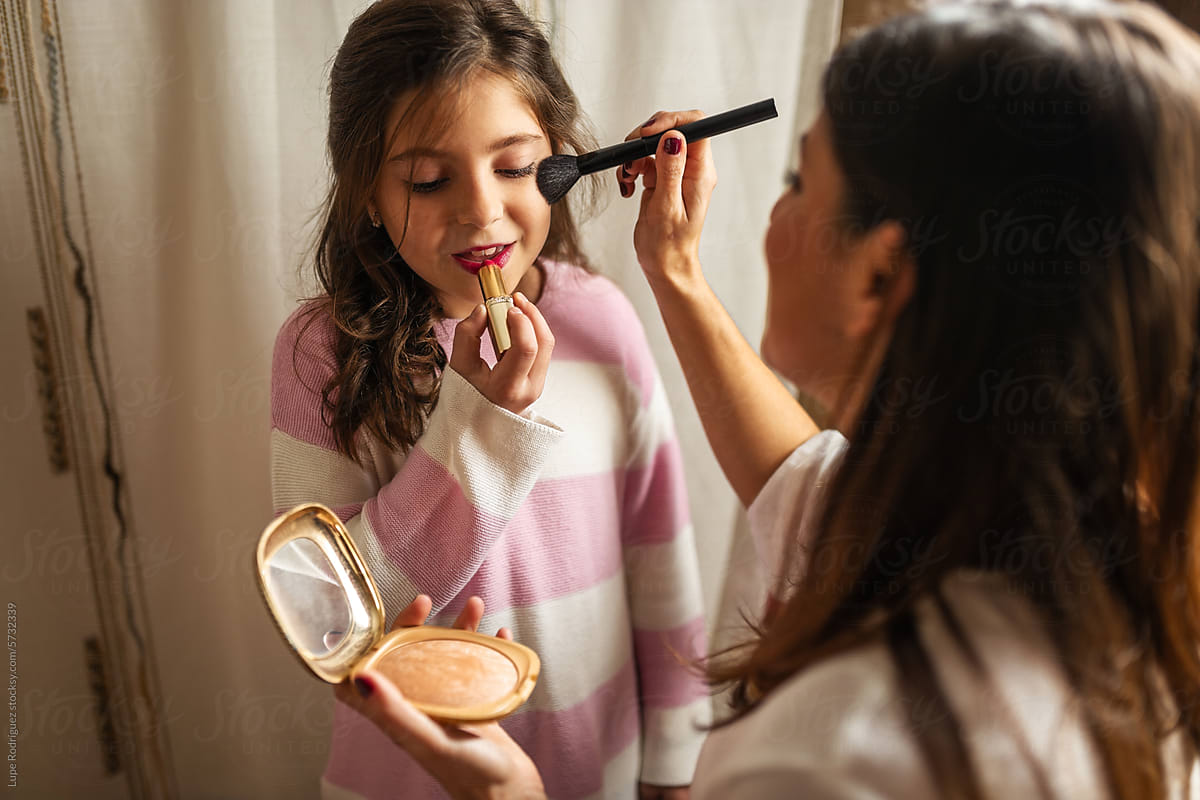 mother putting makeup on her little daughter in the bathroom at home